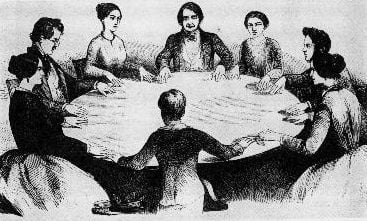 People Gathered round a table holding a seance.
