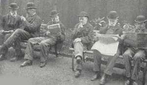 Men reading newspapers and smoking pipes in a Workhouse yard.