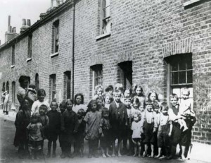 A group of Victorian East Enders gather outside their houses.