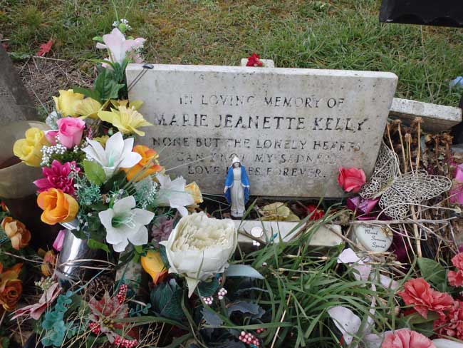 A close up view of Mary Kelly's grave with flowers around the headstone.