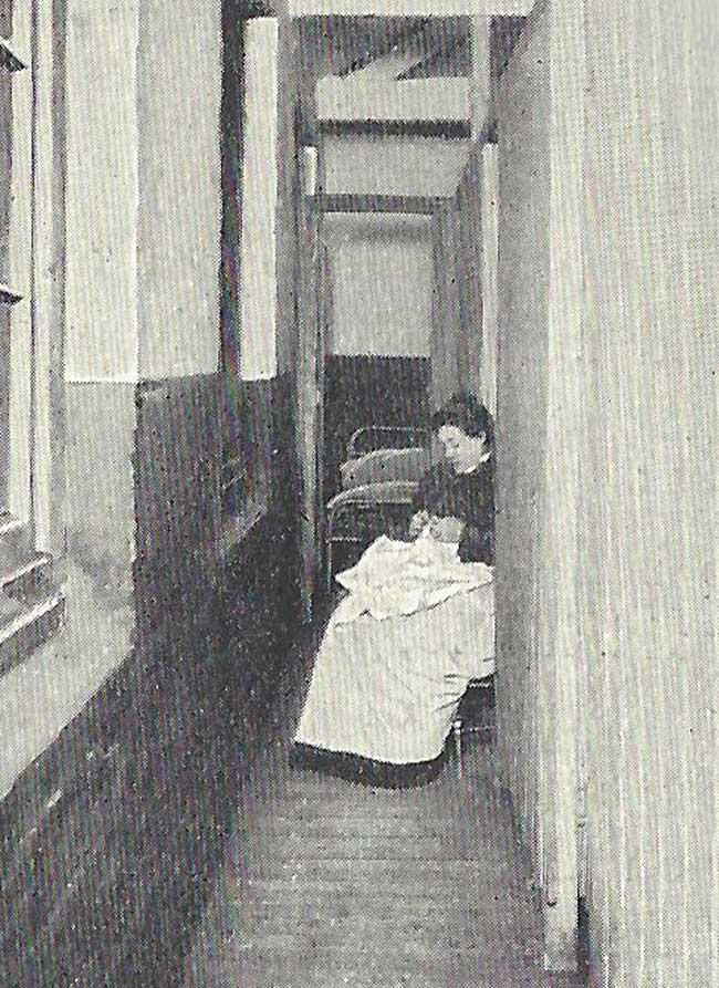 A woma sits by the couples cubicles of a Spitalfields Common Lodging House.