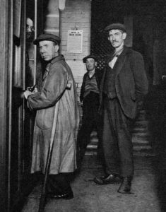Men in coats and flat caps paying thier admission fee for the lodging house.