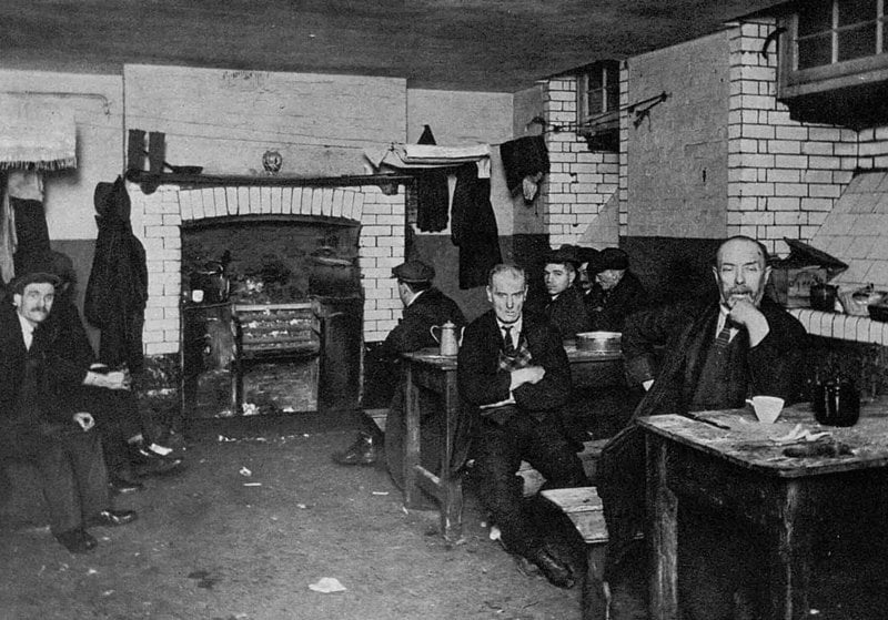 Men sitting at the tables in a lodging house kitchen.