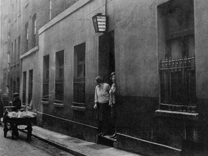 Two women looking out of the doorway of a common lodging house.