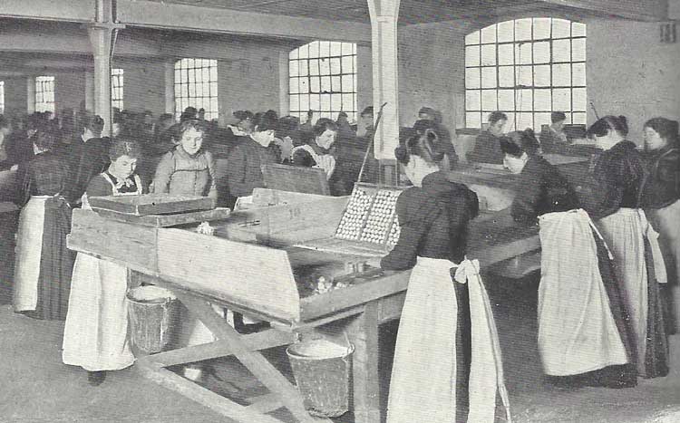 Girls in white aprons working in a factory.